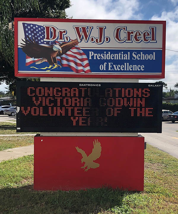 A outdoor sign with an eagle and the American flag on it, displaying the text: Dr. W.J. Creel Presidential School of Excellence, Congratulations Victoria Godwin Volunteer of the Year!