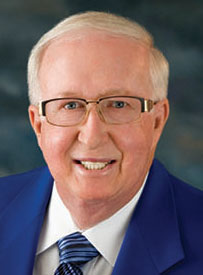 Headshot of Bernie Simpkins, a smiling white man wearing glasses and a blue suit coat with a matching blue striped tie.