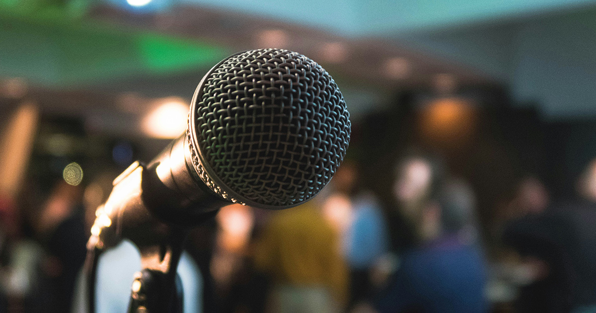 A microphone with a crowd in the background. Like a person standing before a large audience, you can learn to boost your confidence today.