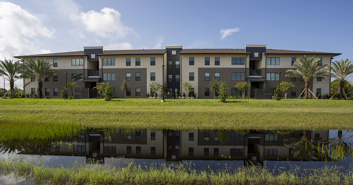 EFSC brown and tan student housing building with palm trees and water in the foreground. The image evokes thoughts about campus living benefits.