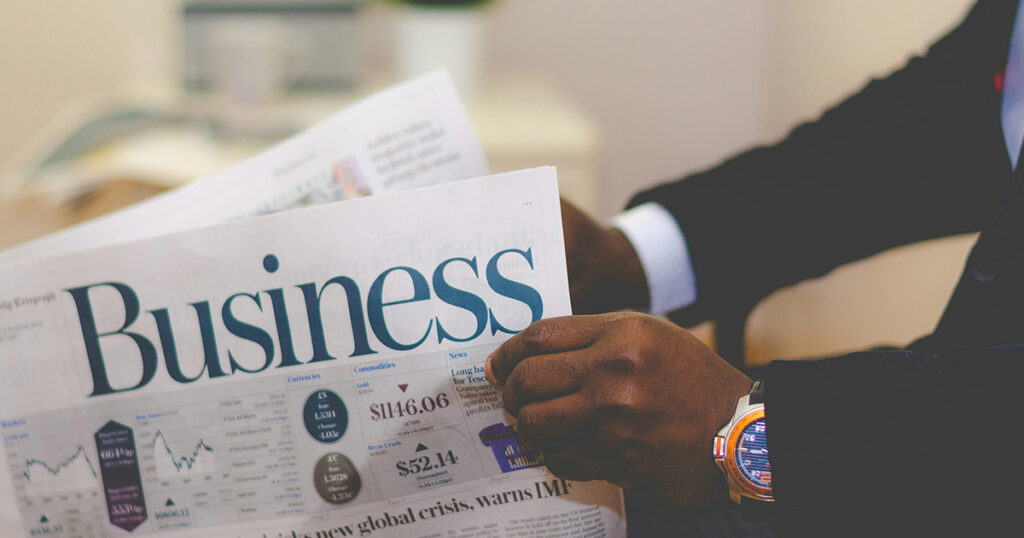 African American man wearing a suit and watch reading the business section of a newspaper. He's putting his college business skills to good use.