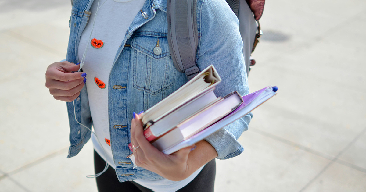 A student holding books wearing a backpack and headphones. she is practicing good college organization tips.