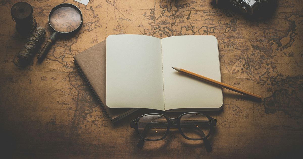 An empty journal and pencil with glasses beneath them. String and a magnifying glass sit to the left of the journal. Under the journal is a rustic map, symbolizing EFSC Academic Success Center resources.