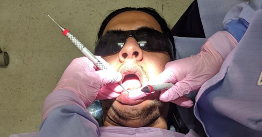 A dental hygiene student cleaning the teeth of a patient wearing dark glasses, Charles Iskander, at the EFSC Dental Clinic.