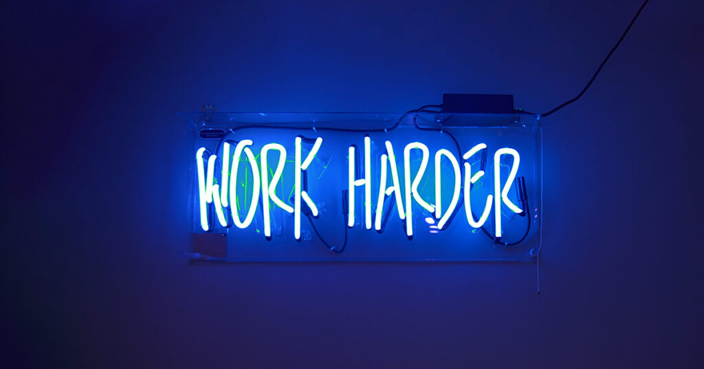 A neon sign with the text "work harder" in blue. It embodies the metaphor of Freshman freedom in college.