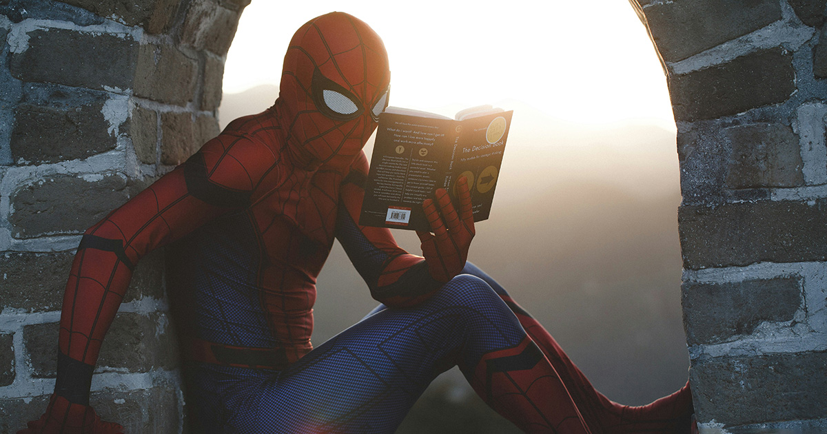 Spider-Man reading a book while bracing between a brick archway. He's practicing ways to get your geek on at EFSC.