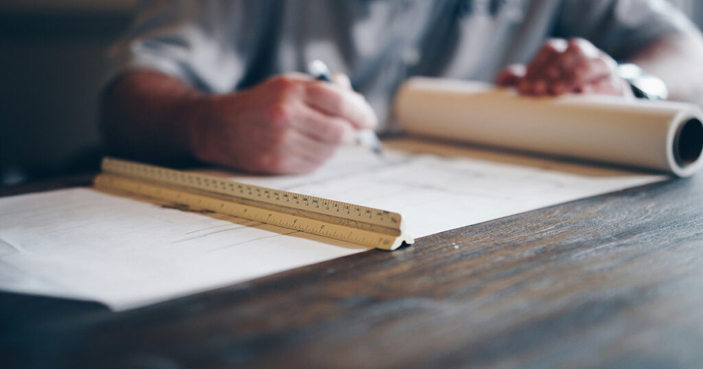 A draftsman making technical drawings with a ruler. The image evokes questions concerning how to become a draftsman.