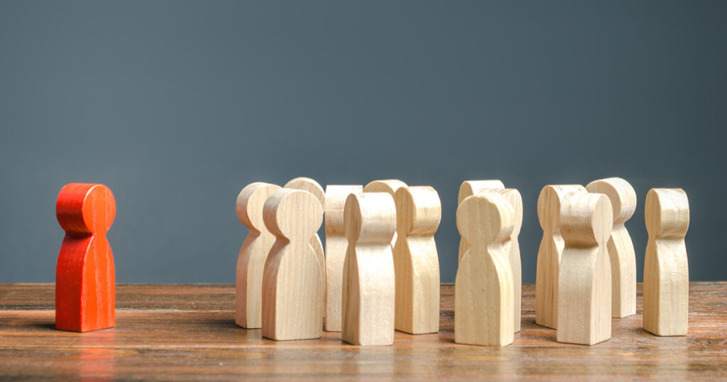 Red figurine of a man stands aside from the crowd of other wooden figurines, representing introvert strengths in college.