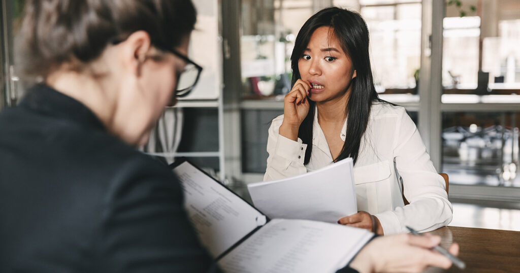 Photo from back of businesswoman interviewing and reading resume of nervous female applicant during job interview - business, career and placement concept. She is working on managing interview anxiety.