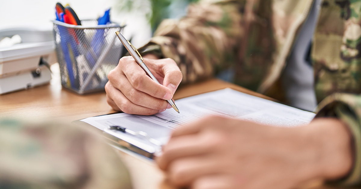 A veteran in camouflage holding a pen filling out a form. He is drawing upon military transition college advice to complete the process.