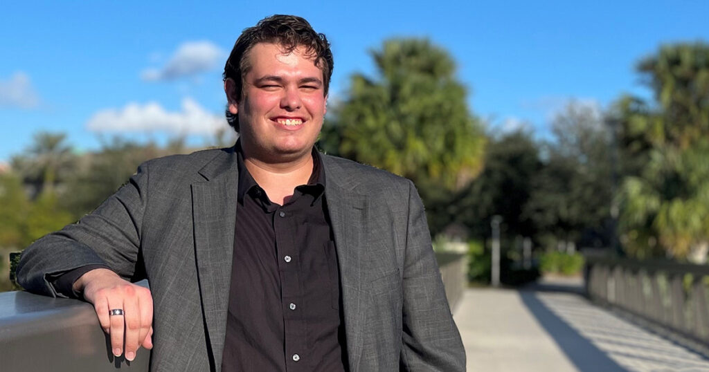 Nick Bath smiling standing on a walkway with trees in the background.