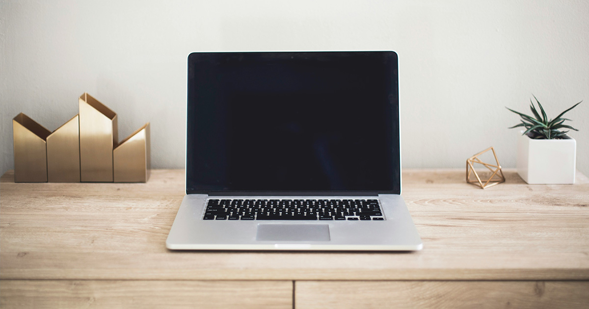 A laptop on a desk. Angular metal art and a plant in a square white pot next to the laptop. The image evokes thoughts of virtual classes and online student success.