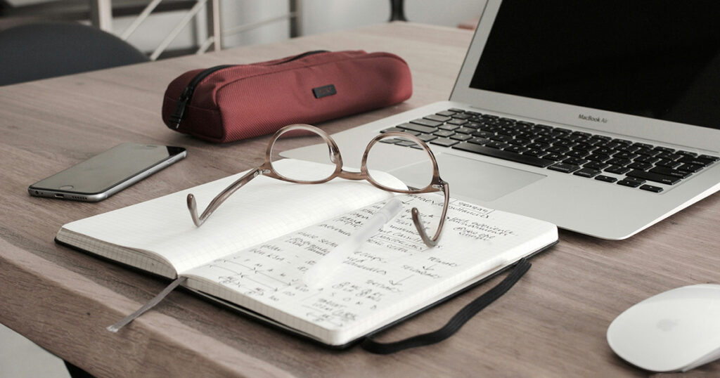 A study space with glasses, a notebook, a laptop, a smart phone, and a pencil case. The perfect setup for discussing the Pell Grant Guide.