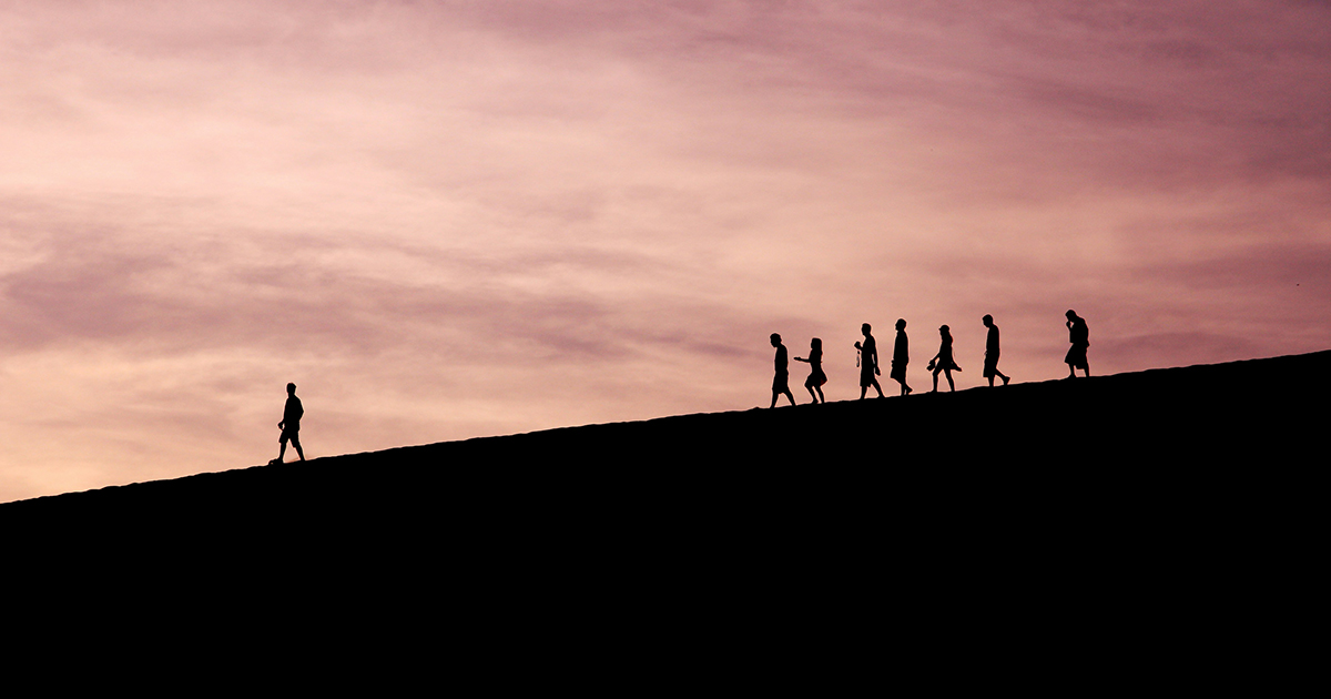 A group of people following a single person leading them down a hill. The image represents persevering through challenging classes.