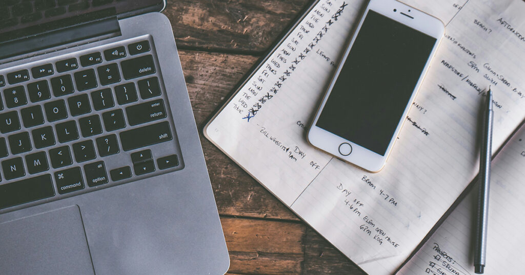 A planner with a smart phone and pen on top of it. A laptop is sitting next to the planner, symbolizing procrastination help for students.