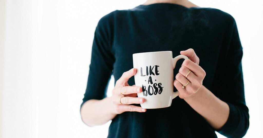 A woman holding a mug that says "Like a boss". It evokes thoughts of working on campus.