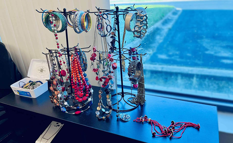 A table in front of a window, with racks on it displaying necklaces and bracelets in different styles.