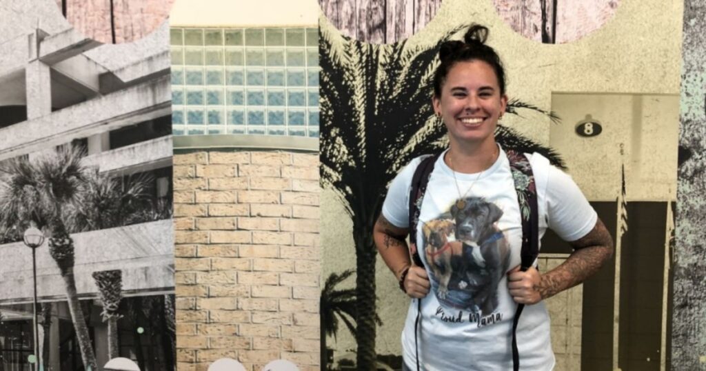 A smiling white woman with dark hair pulled back, earrings, tattoo sleeves, and a T-shirt with dogs on it (Afton Johnson) poses for her EFSC student spotlight.