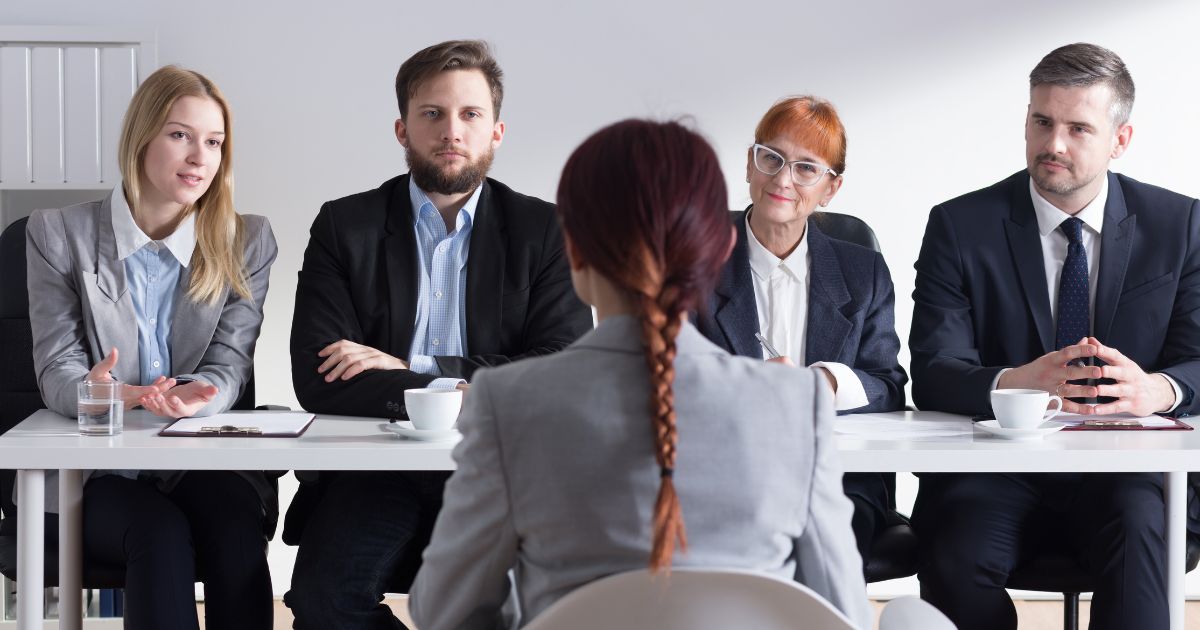 A woman with a braid down her back sits in front of a table with two women and two men in business attire, utilizing EFSC's strong interview tips to get a job.