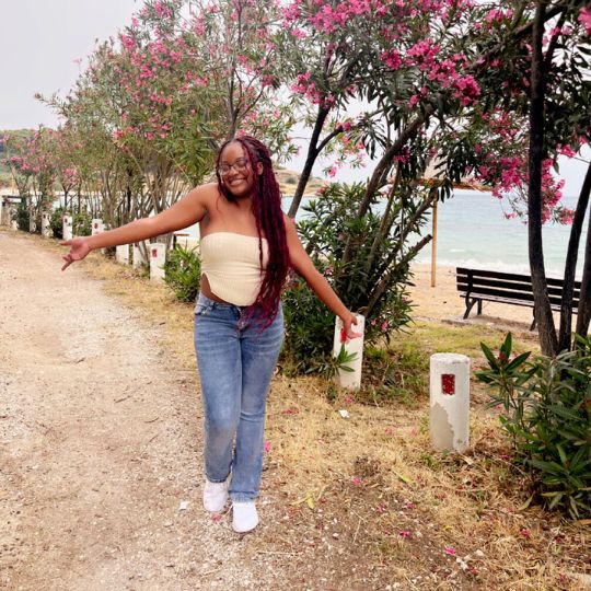 Elysia, a student, stands with outstretched arms and eyes closed enjoying the beauty of an outdoor nature trail.