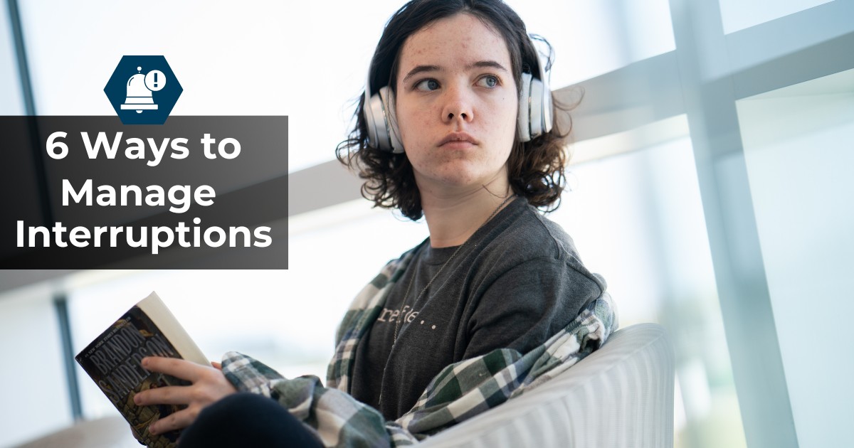 A girl wearing headphones looks over her shoulder from the book she is reading, as though distracted by something.