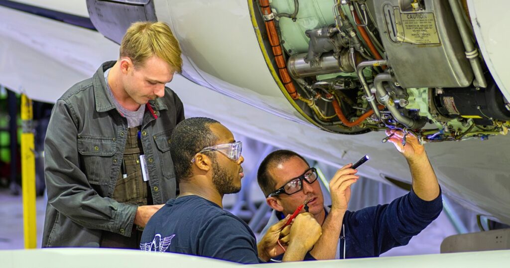 Three diverse aviation technology students work on an aircraft with aircraft tools
