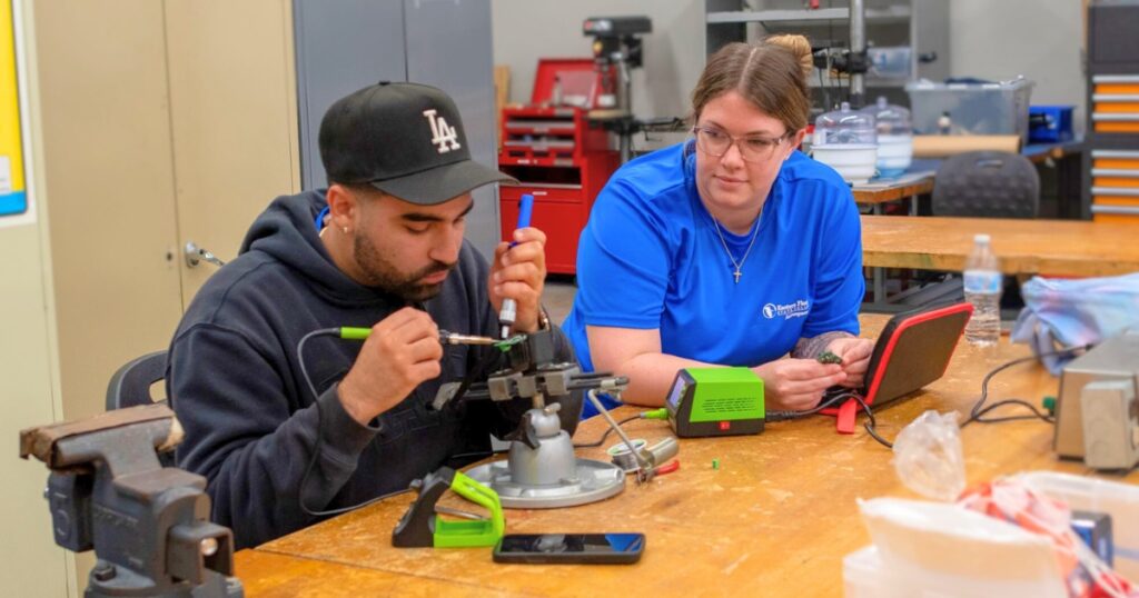 A male and female aerospace technology student work together on a soldering project