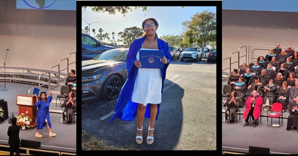 Ary Quinones, a young black woman with glasses wearing a royal black graduation gown blowing in the wind, stands in a parking lot in the shade of a tree holding her diploma case and smiling.