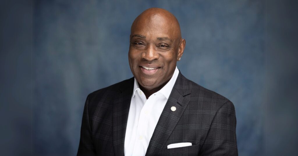 Image of Thomas Highsmith, a bald Black man wearing a black tuxedo with a white dress shirt and smiling at the camera