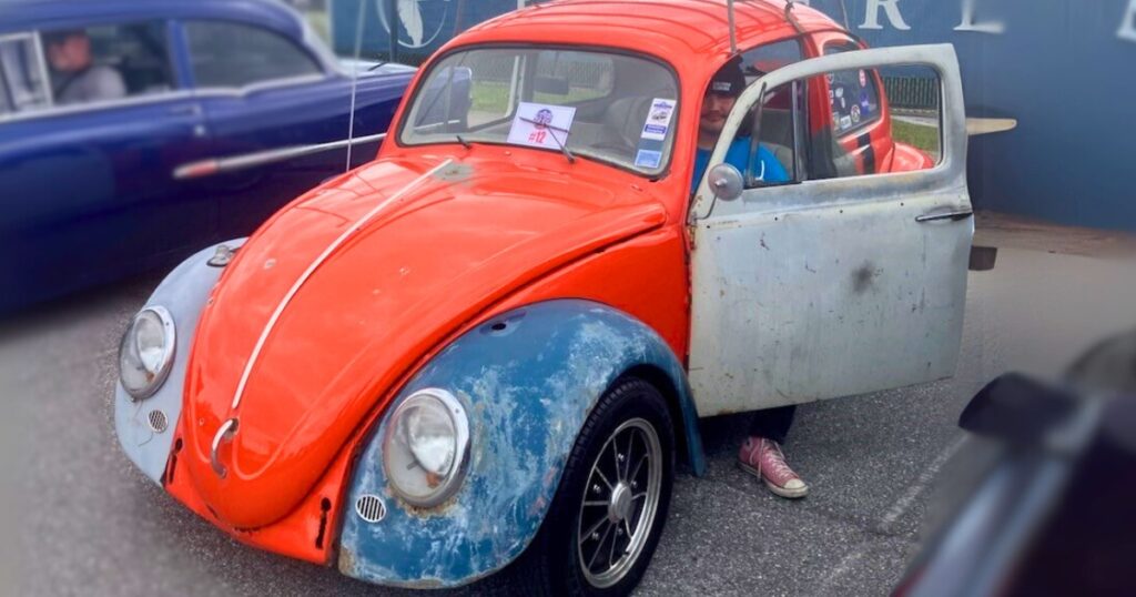 A Volkswagen Type 1 car with an orange body; Tommy Keys sits in the driver's seat wearing an EFSC stocking cap.