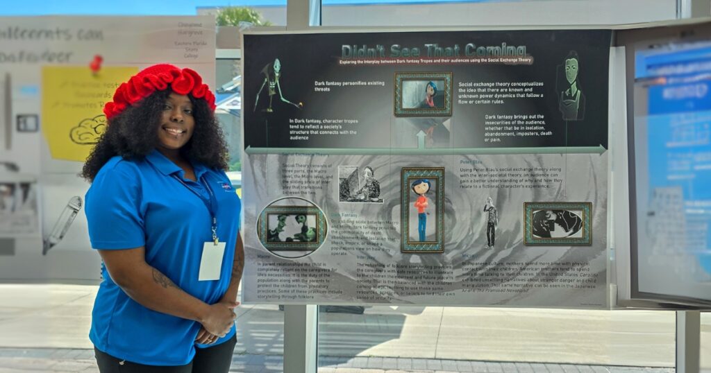 Tynesha Taylor, a young African-American woman wearing a red, knitted hat and blue polo standing by her research poster.