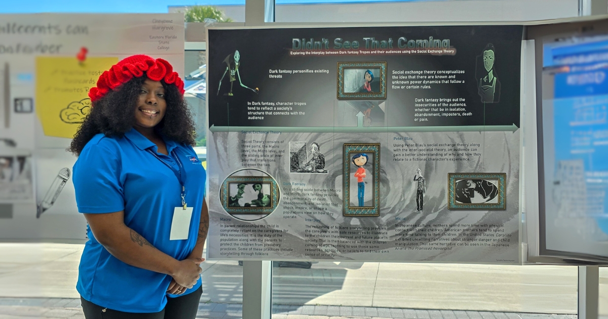 Tynesha Taylor, a young African-American woman wearing a red, knitted hat and blue polo standing by her research poster.