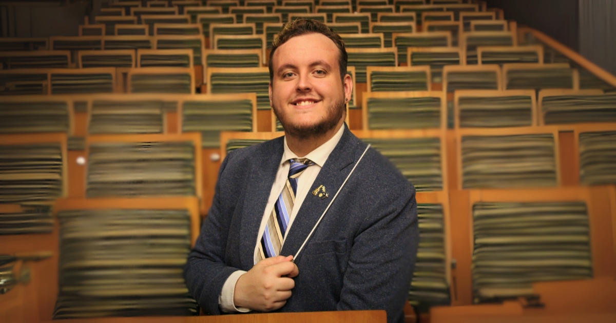 Damian Johnson, a man in a black blazer and striped tie holding a conductors baton