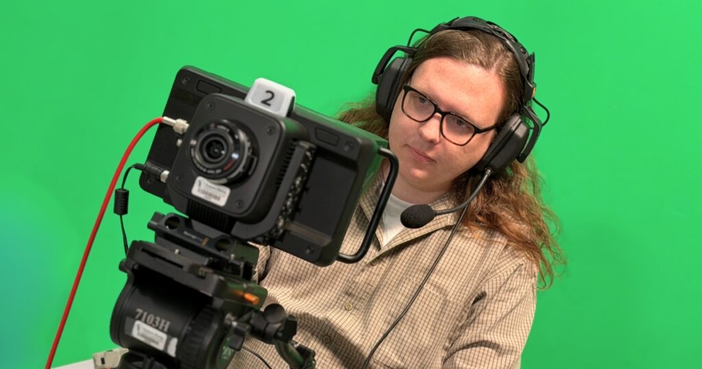 Cameron Web wears headphones while filming in a green screen setting using a professional camera in the Interactive Media program